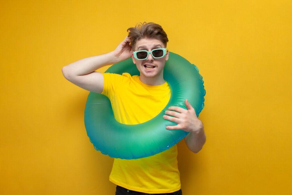 Nachdenklicher Mann mit einem Schwimmring, der sich am Kopf kratzt, auf gelbem Hintergrund