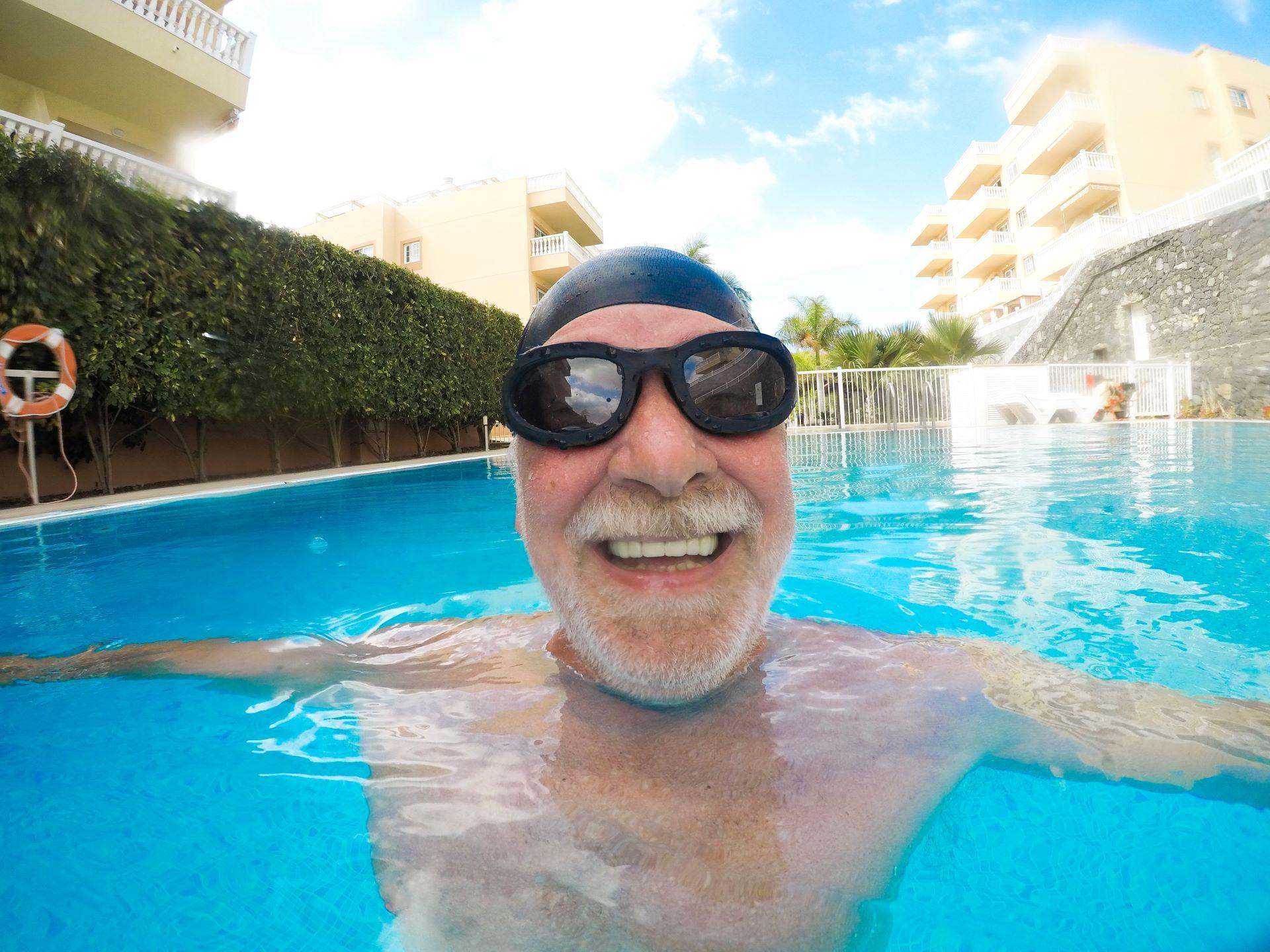 Porträt eines reifen Mannes, der lächelt und in die Kamera schaut, im Schwimmbad, der sich alleine vergnügt - Training und glückliches Schwimmen - Nahaufnahme des Gesichts eines glücklichen Senioren